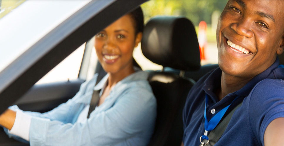 A happy driving school instructor inside a car with a smiling female driving school learner